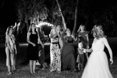 bride in a white dress throws a wedding bouquet to her unmarried girlfriends