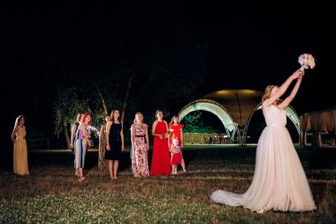 bride in a white dress throws a wedding bouquet to her unmarried girlfriends