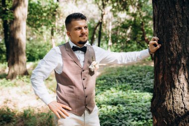 Yeşil ormanın arka planında gri ceketli kel bir adam.