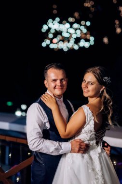 Yeni evli bir çift karanlık bir gökyüzüne karşı havai fişek gösterisi izliyor.