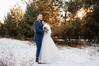 Genç çift, gelin ve damat, karlı bir çam ormanında kış yürüyüşü yapıyorlar.