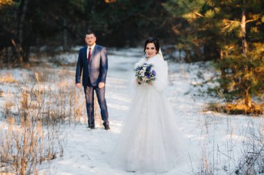 Genç çift, gelin ve damat, karlı bir çam ormanında kış yürüyüşü yapıyorlar.