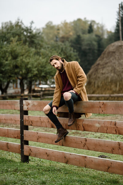 man in a brown coat on a wooden fence