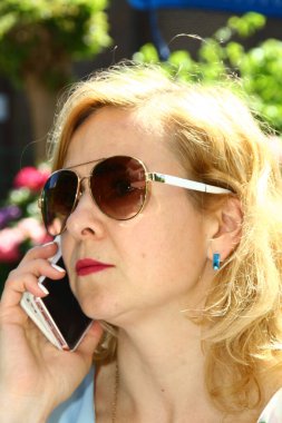 Güneş gözlüğü takan, cep telefonu kullanan bir kadının portresi.