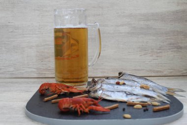 Beyaz arka planda siyah bir tahta var. Bir bardak soğuk bira ve deniz ürünleri değiş tokuş edilen balıklar, kerevitler ve hızlı atıştırmalıklar.