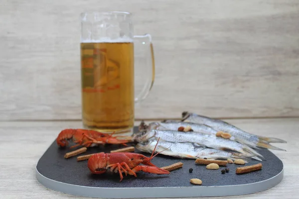 Beyaz arka planda siyah bir tahta var. Bir bardak soğuk bira ve deniz ürünleri değiş tokuş edilen balıklar, kerevitler ve hızlı atıştırmalıklar.