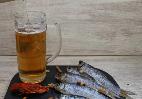 Beyaz arka planda, siyah bir tahta. Bir bardak soğuk bira ve deniz ürününün olduğu yerde. Bira bardaklara doluyor. Balık, kerevit ve atıştırmalıklar. Yukarıdan görüntüle.