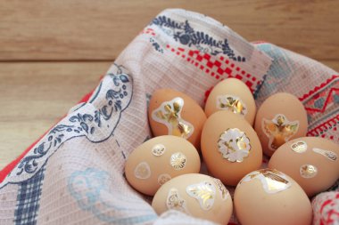 Paskalya çıkartmalarıyla süslenmiş tavuk yumurtaları havluyla kaplı bir sepetin içinde yatıyor.