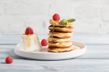 Ahududulu ricotta krepi, beyaz tabakta bal. Yakınlarda ricotta peyniri tareti var. ışık arkaplan, kenar görünüm