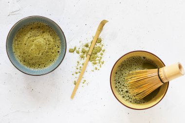 Kasede yeşil çay, dağınık çay tozu ve beyaz arka planda çırpılmış çırpılmış kaşık.