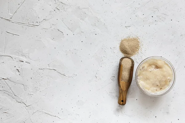 Dry instant yeast in a wooden spoon and a cup with activated yeast — Stock Photo, Image