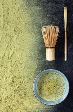 Siyah arka planda serpilmiş yeşil kibrit çay tozu, çırpı ve özel kaşık.