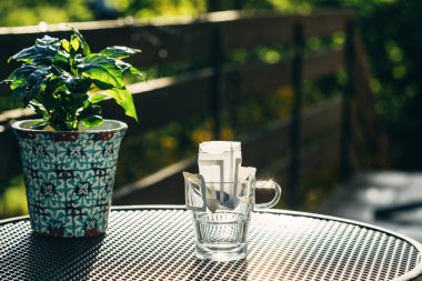 Terasta masanın üzerinde duran, damlayan kahve torbası olan temiz bir cam bardak.