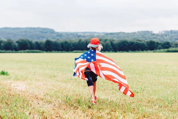 Little boy runs across the field, holds a waving American flag — Stock Photo, Image