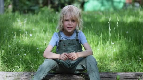 Calm happy blonde child sits on a bench, smiles and laughs — Stock Video