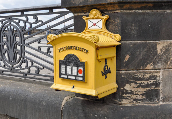 classic decorative yellow postbox attached to historic sandstone balustrade in Dresden's picturesque old town.