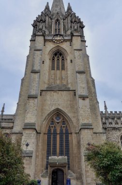 View of english gothic building facade and sky of University Church of St Mary the Virgin Tower with ogival arched windows and intricate architectural detailing from Oxford High Street, Oxford, United Kingdom.