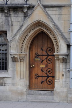 View of english gothic building facade with ogival arched wooden door and intricate architectural detailing from Oxford High Street, Oxford, United Kingdom.