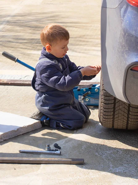 A little boy fixes a car, changes a wheel, helps his dad. — Stock Photo, Image