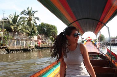 Uzun saçlı esmer kız tekneyle Bangkok kanallarından geçiyor.