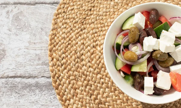 Concept de cuisine méditerranéenne. Salade grecque dans un bol blanc sur le support en paille tricotée. — Photo