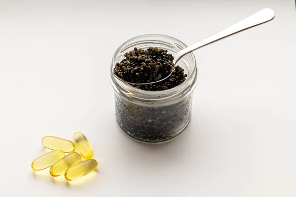 Caviar negro y cápsulas de vitaminas sobre un fondo blanco con un espacio de copia. —  Fotos de Stock