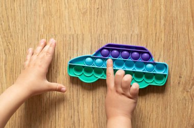 Çocuk pop it oyuncağıyla oynuyor. Ahşap arka planda basit bir gamzeli oyuncak.