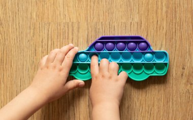 Çocuk pop it oyuncağıyla oynuyor. Ahşap arka planda basit bir gamzeli oyuncak.