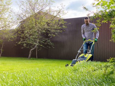 Genç bir adam çim biçme makinesiyle bir çim biçer. Bahçede yaz çalışması