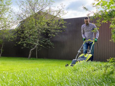Genç bir adam çim biçme makinesiyle bir çim biçer. Bahçede yaz çalışması