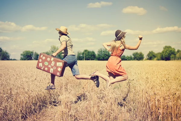 Couple running in field, man holding in his hand vintage suitcase on countryside landscape blue sky outdoors background — Stock Photo, Image