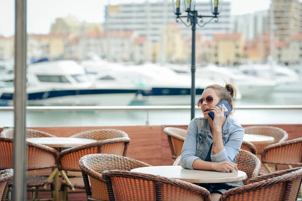 Veselý šťastný usmívající se krásná žena mluvit pomocí smartphone v restauraci na pozadí marina luxusní. Koncept - křížovky, cestování — Stock fotografie