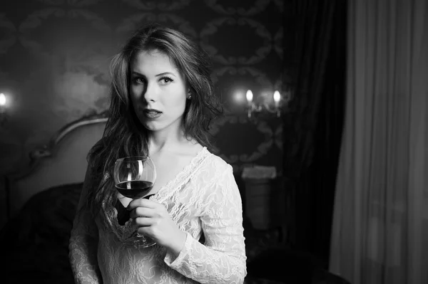 Fotografia in bianco e nero di bella signorina con un bicchiere di vino in camera da letto di lusso — Foto Stock