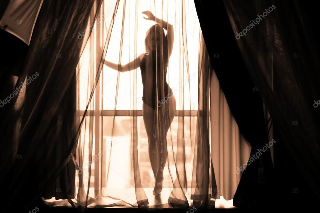 Sexy beautiful young lady relaxing over light window background. Black and white