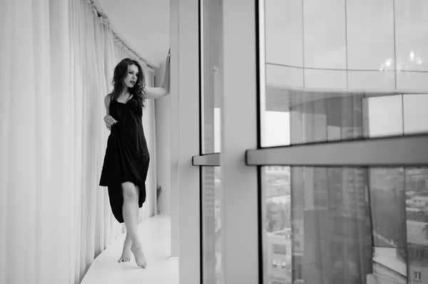 O tânără frumoasă se relaxează uitându-se pe fereastră. Imagine alb negru — Fotografie, imagine de stoc