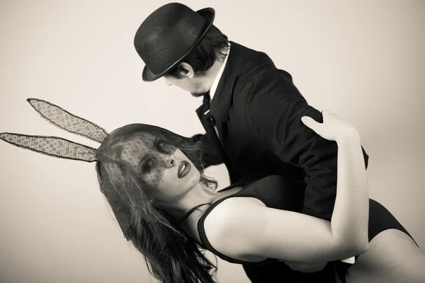 Černobílá představa sexy krásné mladé dámy s králíky tančící s mužem v klobouku na světlém pozadí — Stock fotografie