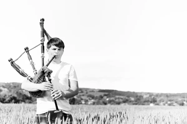 Black white photography of man enjoying playing pipes in Scottish traditional kilt on green outdoors copy space summer field — Stock Photo, Image