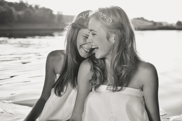 Black white photography of two happy girls playing in water at the sunset beach. Sun flare background — Stock Photo, Image