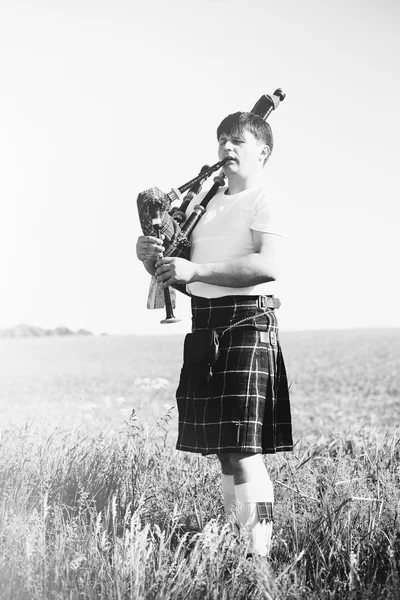 Black white photography of man enjoying playing pipes in Scottish traditional kilt on outdoors copy space summer field — 스톡 사진