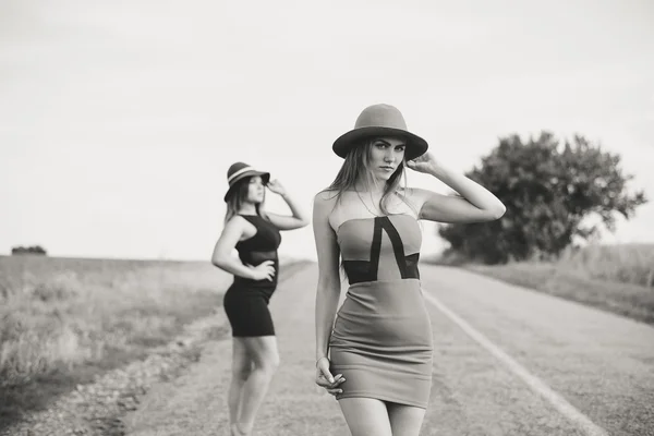 Fotografía en blanco y negro de dos hermosas chicas elegantes en sombreros, soleado fondo de día de verano al aire libre — Foto de Stock