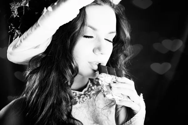 Black and white photography of young beautiful woman in classical clothes eating chocolate with eyes closed, closeup portrait