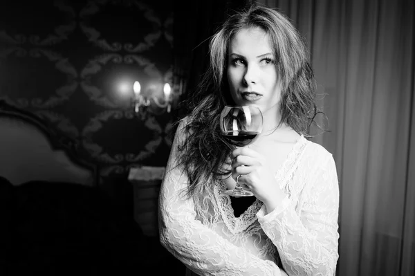 Fotografía en blanco y negro de una hermosa joven con una copa de vino en el dormitorio de lujo — Foto de Stock