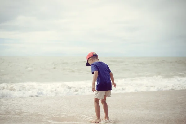 Vue arrière du petit garçon marchant le long de la plage pendant le coucher du soleil — Photo