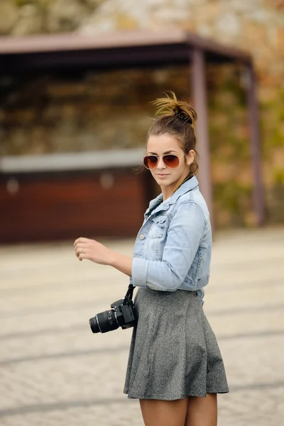 Mulher turística jovem atraente visitando uma rua de seixos com monumento de parede de pedra texturizada, girando para sorrir para a câmera em umas férias de verão, ao ar livre . — Fotografia de Stock