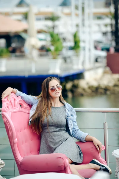Portrait of beautiful young lady in sunglasses sitting in elegant armchair. — Stock Photo, Image