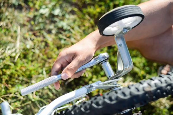 Closeup on hands of male fixing mechanism of the bicycle, green background outside — Stock Photo, Image