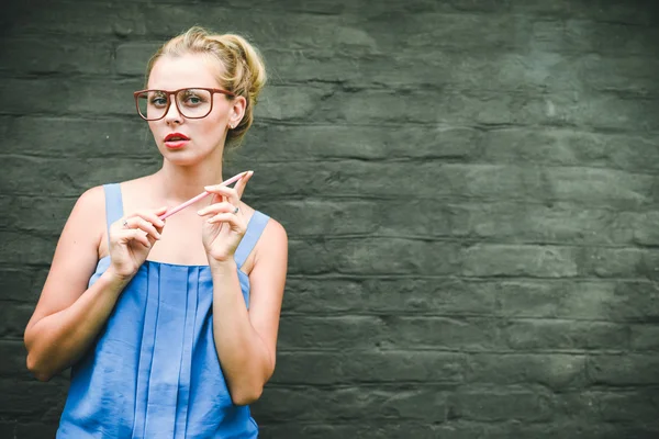 Clever smiling blonde beautiful female holding pencil on grey wall background — Stock Photo, Image