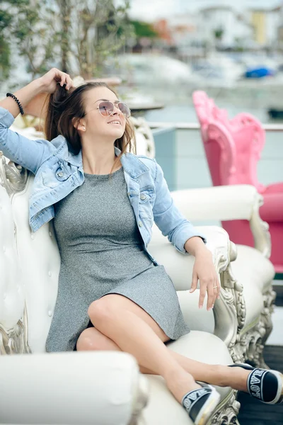 Portrait of beautiful young lady in sunglasses sitting in elegant armchair. — Stock Photo, Image