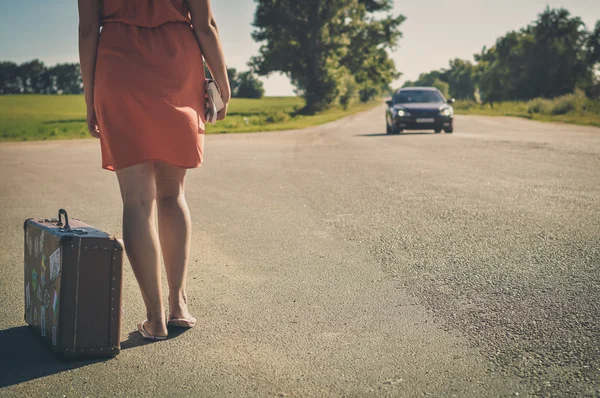 Rückansicht einer jungen hübschen Frau, die per Anhalter entlang der Straße auf eine Fahrt wartet — Stockfoto