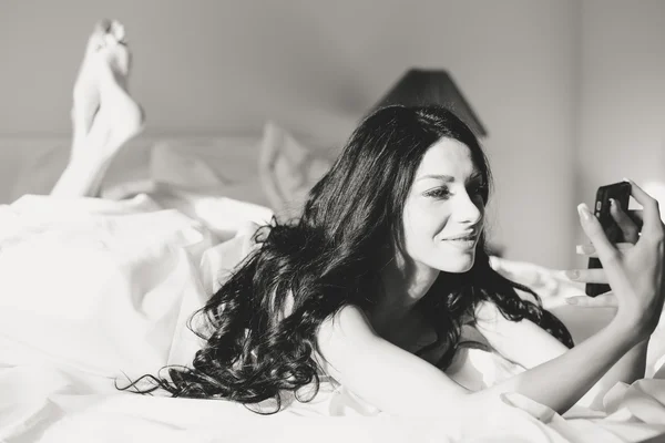 Selfie を取って、スマート フォンを使ってベッドに敷設いちゃつく若い女性の肖像画 — ストック写真